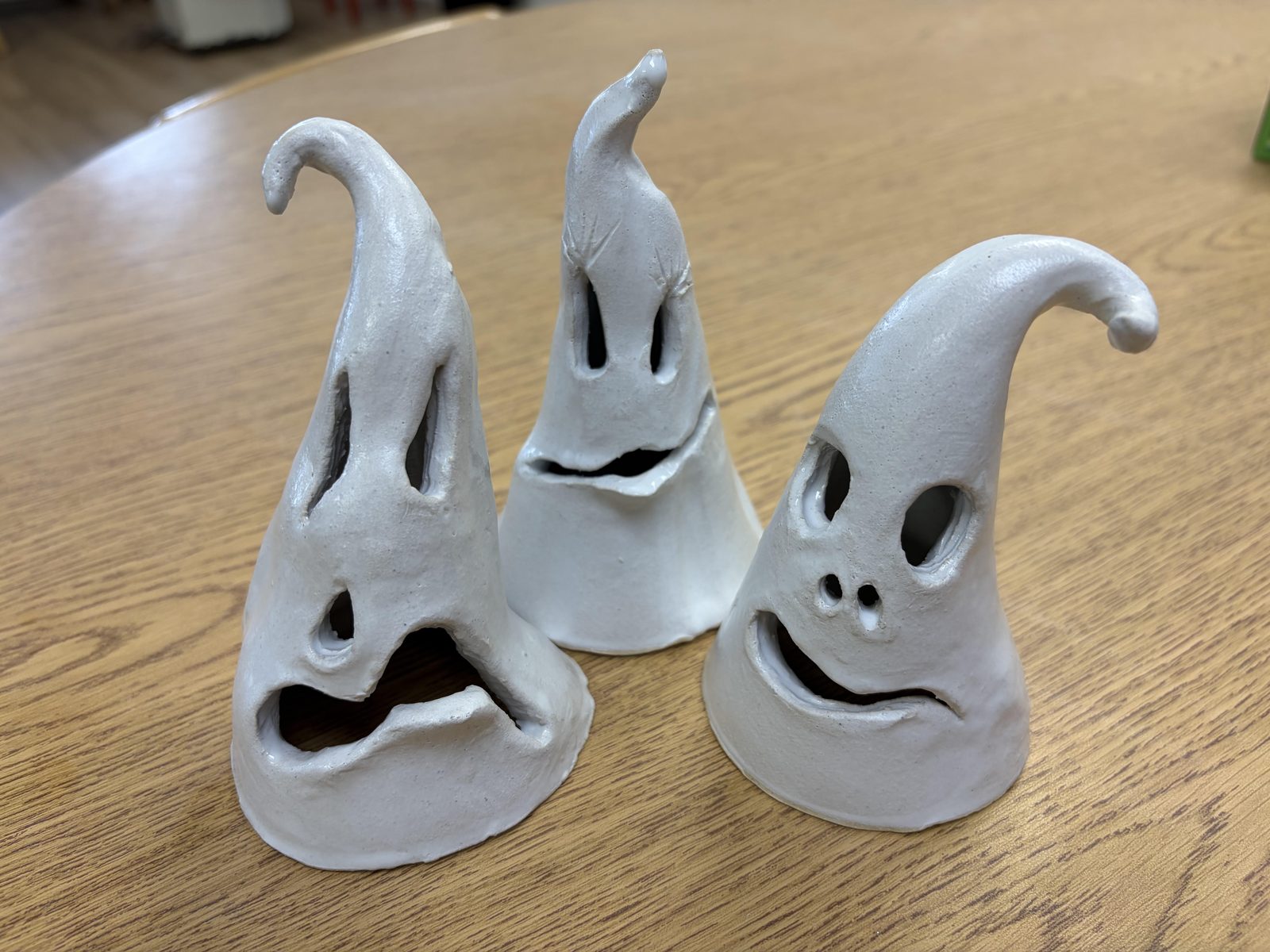 Three finished clay ghosts with carved faces, bisque fired, on a wooden table