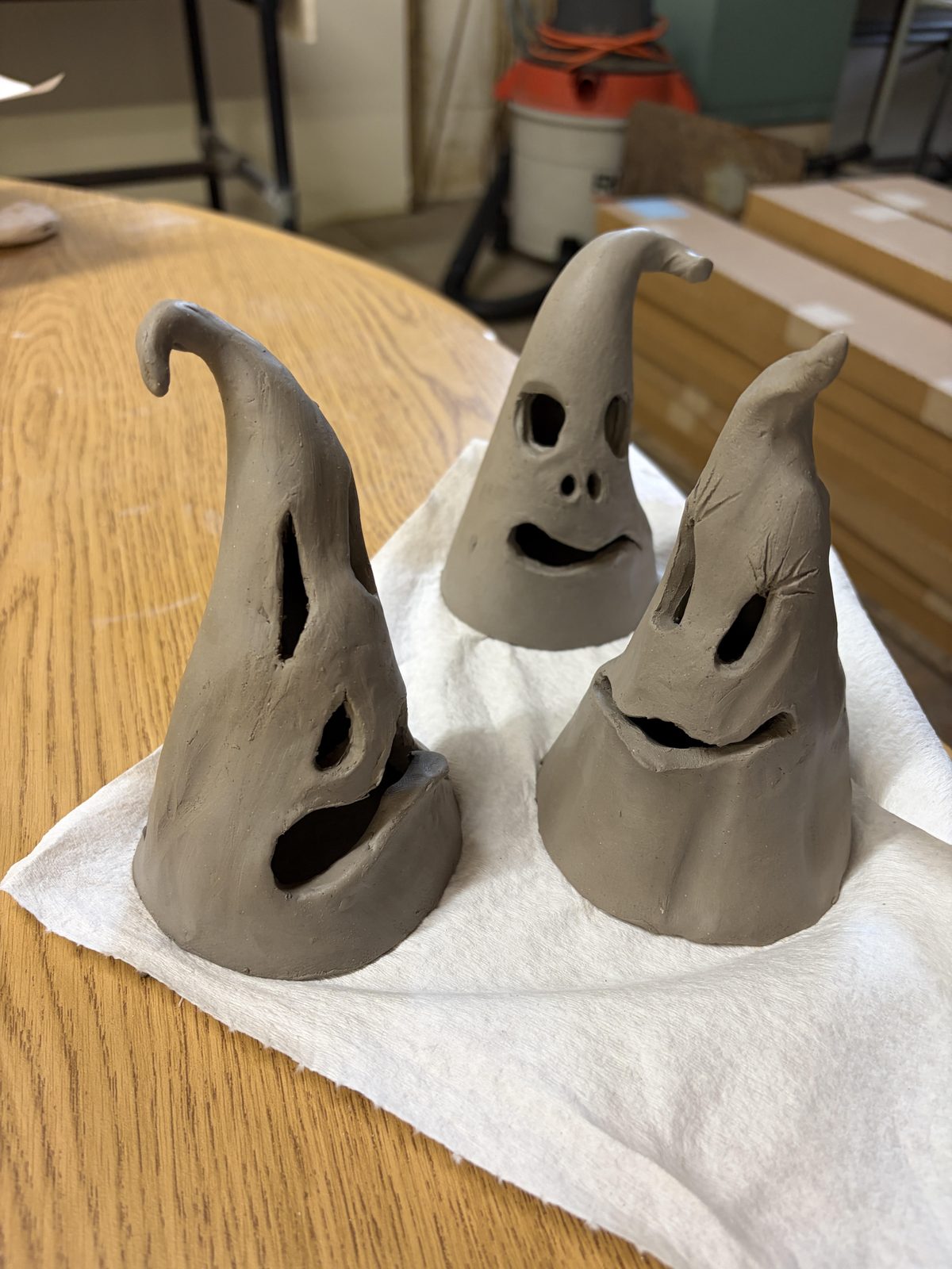 Three ghosts being built from grey slab clay, drying on a cloth in the studio