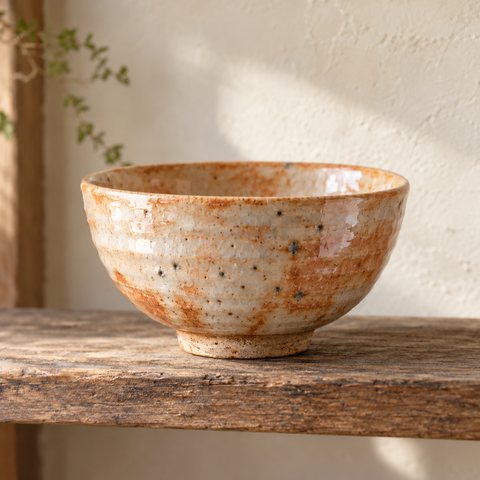 A bowl in warm orange and creamy white shino, freckled with dark pinholes.