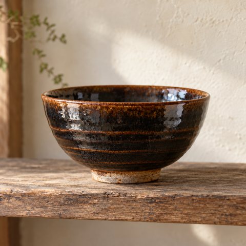 A near-black glossy bowl, the glaze breaking to rust brown along the rim.